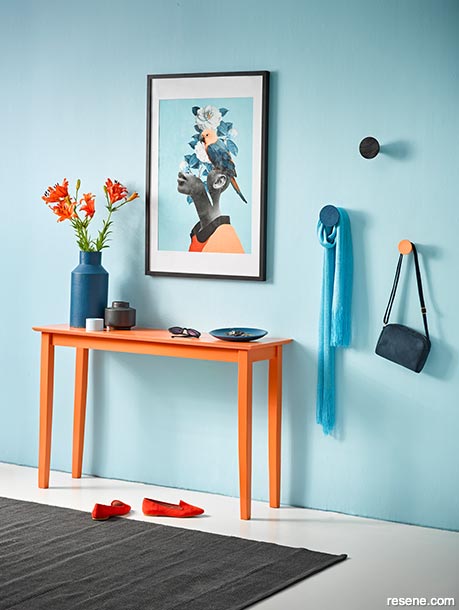 A sleek orange hall table in a light blue hallway